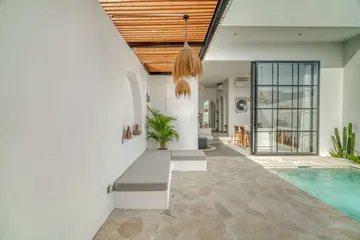 Covered stone terrace with built-in bench, timber ceiling slats and glass entry doors.