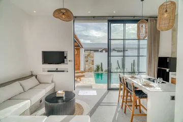 Sectional sofa and television beside a dining island set with glasses, with the courtyard through glass.