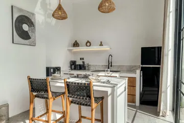 Kitchen counter with dark woven chairs, open shelving and a black refrigerator.