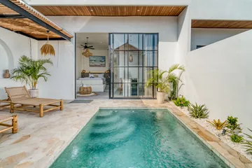 Turquoise courtyard pool with pale stone paving and a row of loungers.