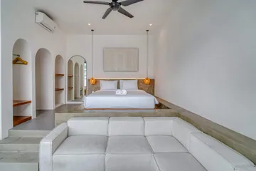 Low bed behind a pale sectional sofa, with arched niches and a ceiling fan.