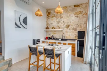 Dining table and kitchen beneath woven pendants, with abstract artwork on a pale wall.