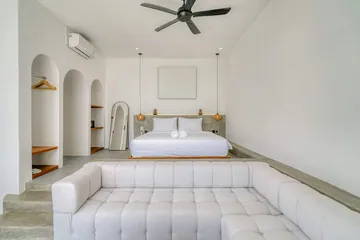 Bedroom with white bed and sectional beneath a ceiling fan.