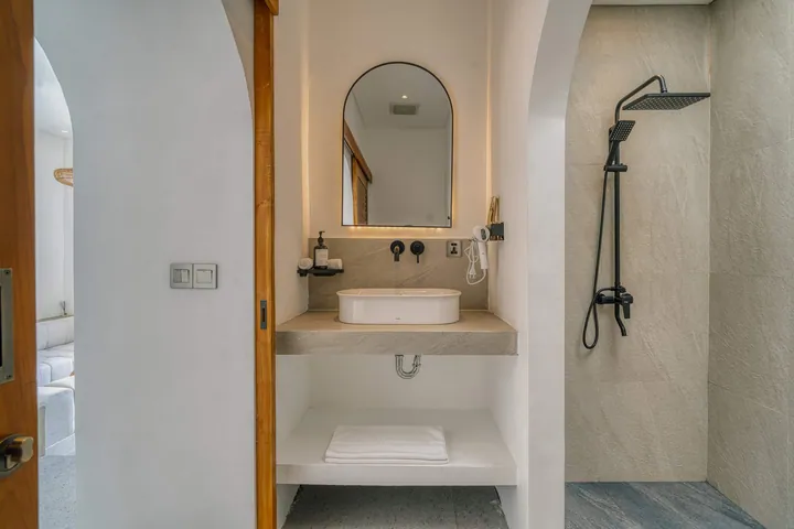 An arched bathroom mirror, pale stone basin and timber detailing.