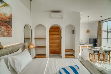 Bed in the foreground with an arched mirror, arched timber door and kitchen counter beyond.