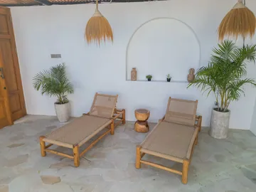 Two wooden loungers and a low table in a bright alcove with potted greenery.