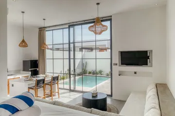 Living area with sectional sofa, wall-mounted television and dining island beside glass doors to the pool.