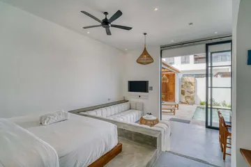 White bed and sectional viewed from the side, with glass doors to the courtyard.