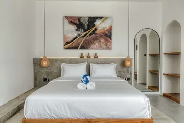 Close view of a made bed beneath abstract artwork, with arched wall niches and bedside pendants.