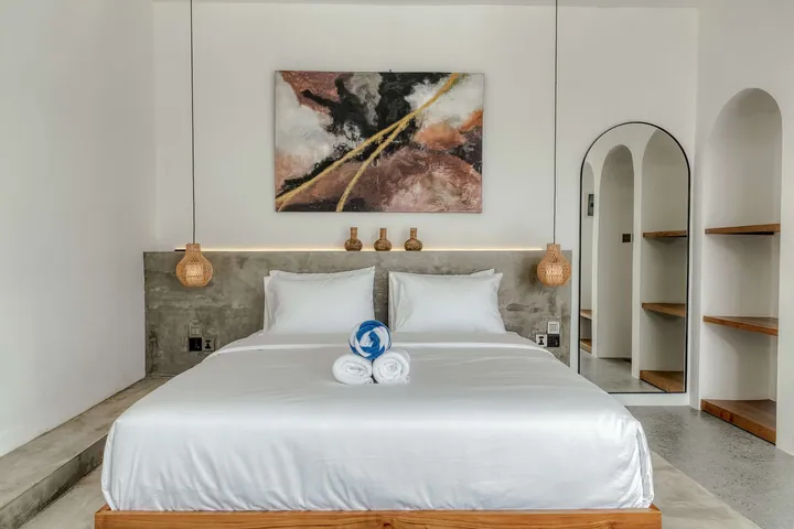 Close view of a made bed beneath abstract artwork, with arched wall niches and bedside pendants.