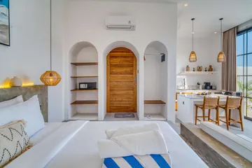 Bedroom with arched wood door, built-in niches, white bed and compact dining counter beyond.
