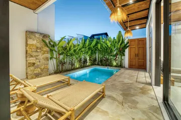 Courtyard pool with woven loungers, a stone feature wall and a timber door at dusk.