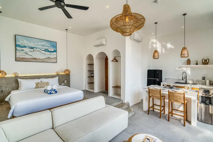 Open-plan room with low bed, sectional sofa and pale stone kitchen wall.