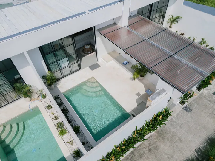 Aerial view of a courtyard pool, white roof and surrounding planted border.