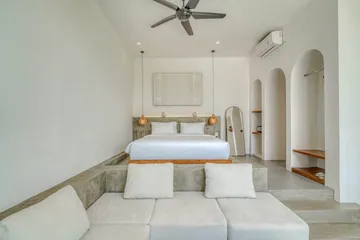 Low bed centered beneath a framed coastal artwork, with arched niches and a ceiling fan.