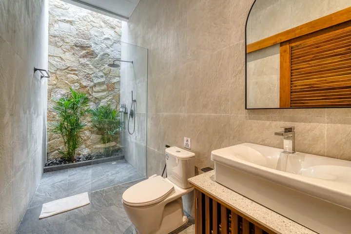 Open-air shower and vanity beside a stone wall and wood-framed mirror.
