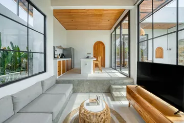 Pale seating and a television beneath a timber ceiling, beside floor-to-ceiling windows.