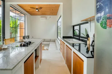 Long kitchen counter with wood-front cabinets, cooktop and island stools.