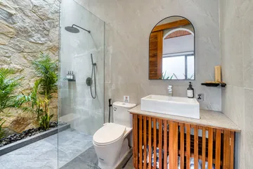 Compact bathroom with toilet, vanity and shower against pale stone walls.