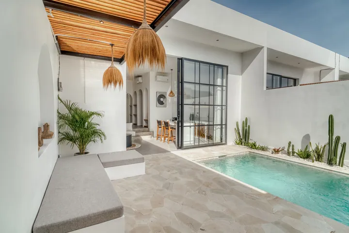 Courtyard pool framed by pale walls, timber roof slats and green planting.