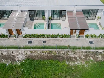 Aerial view of a white villa row and planted borders along a paved lane.
