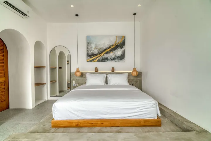 Low bed beneath abstract artwork, with arched doorways, wall niches and an arched mirror.