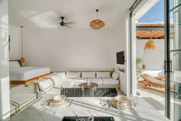 Open-plan room with a low bed, sectional sofa and a dining table with place settings.