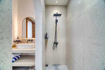 Stone vanity with a vessel basin and arched mirror beside a walk-in shower.