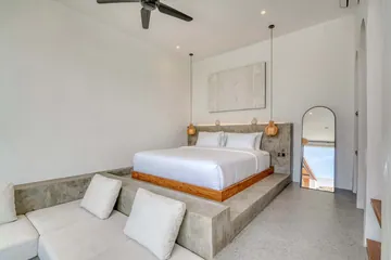 Low bed on a stone platform beside an arched mirror and sectional sofa.
