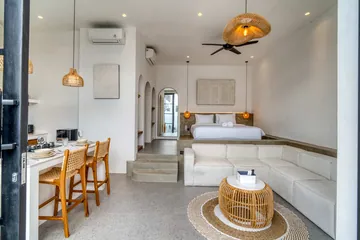 Open-plan living and dining area with a sectional, set table, kitchen and low bed.