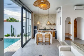 A kitchen and dining island beside tall black-framed glass doors opening towards a pool.