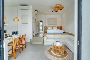 View across the sectional sofa toward a low bed, kitchen counter and tall glass doors.