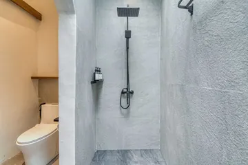 Pale stone shower enclosure with a dark rainfall shower head and controls.