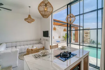 Open-plan room with white bed, sectional and a compact kitchen.
