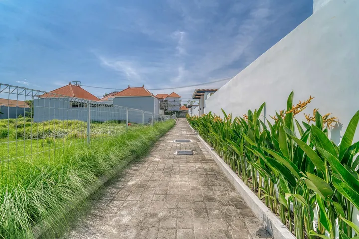Straight paved path bordered by low walls and open green fields.