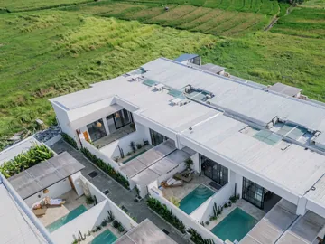 Aerial view of a row of white villas and small courtyard pools amid green fields.