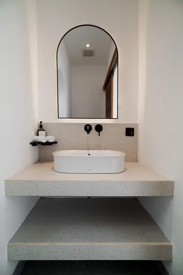 Pale stone vanity with a vessel basin, black wall tap and mirror above.