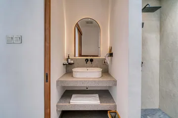 An arched bathroom mirror, pale stone basin and timber detailing.