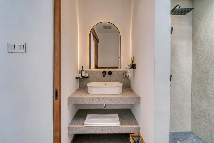 An arched bathroom mirror, pale stone basin and timber detailing.