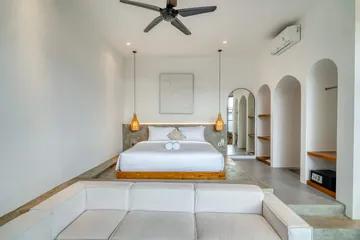 Low bed and sectional sofa beneath a ceiling fan, with arched niches along the wall.