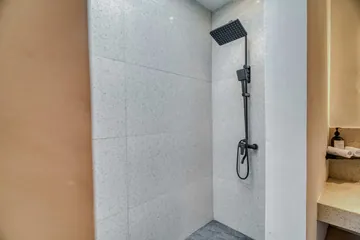 Compact bathroom with stone shower, toilet and vanity beside a wood slatted door.