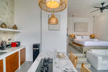Kitchen island set for dining, with cooktop, wood-front cabinets and a bed beyond the sofa.