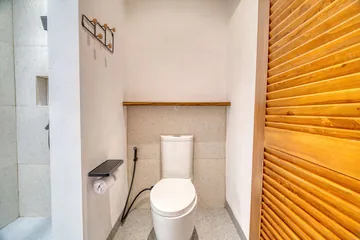 Toilet beside a louvred timber door in a pale bathroom.