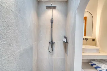 Walk-in shower with a dark rain-style showerhead beside a stone vanity and arched mirror.
