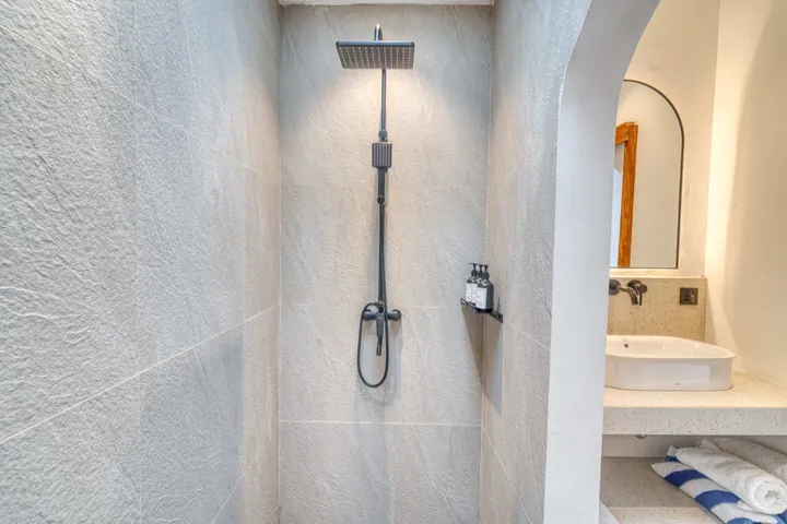 Walk-in shower with a dark rain-style showerhead beside a stone vanity and arched mirror.