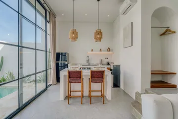 Kitchen counter with dark woven stools beside full-height glazing and an arched doorway.
