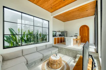 White sectional and wood coffee table beside a large window under timber ceiling.