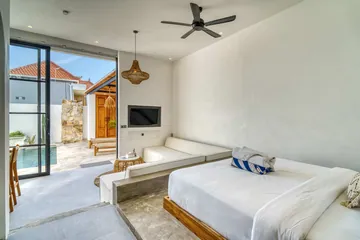 Bedroom with a white bed beside a low built-in bench and sliding glass doors to a paved patio.