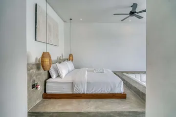 Low bed on a timber platform beside a stone ledge, beneath woven pendants.