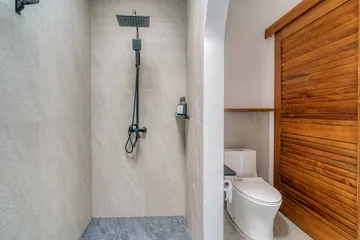 Compact bathroom with stone shower, toilet and a wood slatted door.
